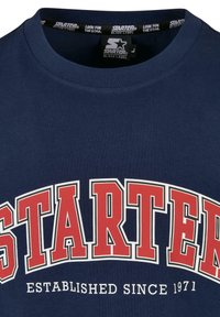 Námořnická modrá bavlněná tričko s velkým červeným a bílým nápisem "STARTER" a potiskem "ZALOŽENO V ROCE 1971". Klasický kulatý výstřih.