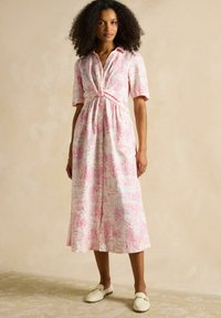 Rozā un baltā rakstainā kleita ar īsām piedurknēm, sasietu priekšpusi un plūstošu svārku. Pārdota ar baltām slīdējošām botām.