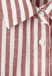 Chemise à col avec des rayures verticales rouges et blanches, avec deux boutons blancs attachés le long de la patte de boutonnage avant.