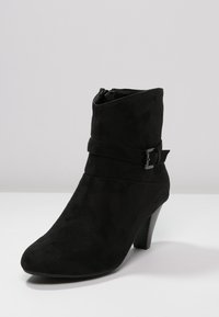 Černá semišová kotníková bota se špičatou špičkou, bočním zipem a dekoračním páskem s kovovou sponou. Černý blokový podpatek.