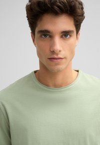 Hellgrünes Baumwoll-T-Shirt mit rundem Ausschnitt und kurzen Ärmeln. Glatte Textur, schlichtes Design, keine sichtbaren Muster oder Grafiken.