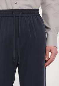 Tummansininen housut, joissa on elastinen vyötärö ja nauha. Sileä kangas, jossa on hienovarainen rakenne, ja sivutaskut sekä rento istuvuus.