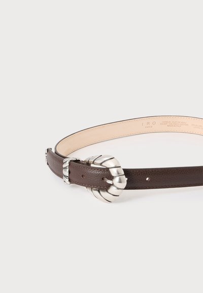 Ceinture en cuir marron avec une grande boucle en métal argenté torsadé et passant assorti sur fond uni clair.