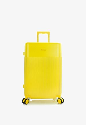 Valise rigide jaune vif avec moitié inférieure texturée, poignée rétractable et quatre roues doubles pivotantes sur fond blanc.