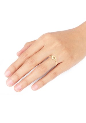 Gold ring featuring a floral design and an open band, resting on a hand with natural nails, set against a white background.