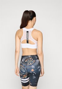 Biely športový podprsenka s sieťovaným chrbtom a textom "STRONGER". Čierne šortky s farebnými abstraktnými vzormi a bielymi pruhmi. Úzky strih.