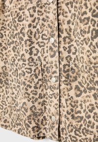 Camicia in denim con stampa leopardata, caratterizzata da bottoni a pressione metallici, due tasche frontali e un tessuto morbido e texturizzato nei toni beige e marrone.