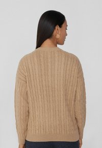 Beige Kabelstrickpullover mit geripptem Saum und Bündchen, der eine lockere Passform und ein strukturiertes Muster auf der Rückseite aufweist.