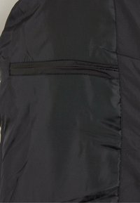 Schwarze Oberbekleidung aus einem weichen Stoff, mit einer kleinen, mit Reißverschluss versehenen Tasche und flachen Nähten für ein elegantes Erscheinungsbild.