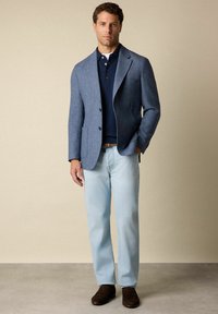 Světle modré denimové džíny v kombinaci s námořnickým modrým polo tričkem a texturovaným, světle modrým saka. Hnědé boty doplňují tento outfit.