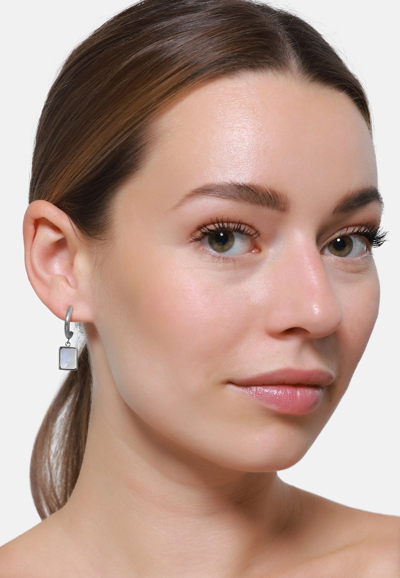 Sølv hoop-øreringer med en rektangulær, semi-transparent anheng, med en polert overflate og glatte kanter, båret i en models øre.