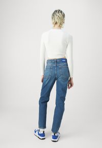 Top blanco de manga larga con textura acanalada combinado con vaqueros de cintura alta de mezclilla azul. Las zapatillas presentan acentos azules y la marca "HUGO" en el lateral.