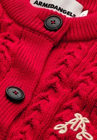 Roter Strickcardigan mit einem Kabelstrickmuster, schwarzen Knopf und besticktem Design. Die Textur ist dick und gemütlich, ideal zum Layering.