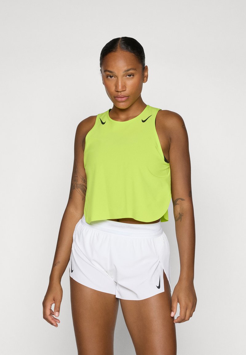 Neon grøn cropped tank top med rund halsudskæring og sort Nike-logo, kombineret med hvide træningsshorts med sorte detaljer.