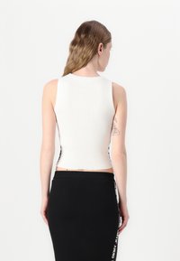 Hvit ribbestrikket tanktop med en tettsittende design, med rund hals og sidesømmer. Kombinert med et svart tettsittende skjørt med merkevare.