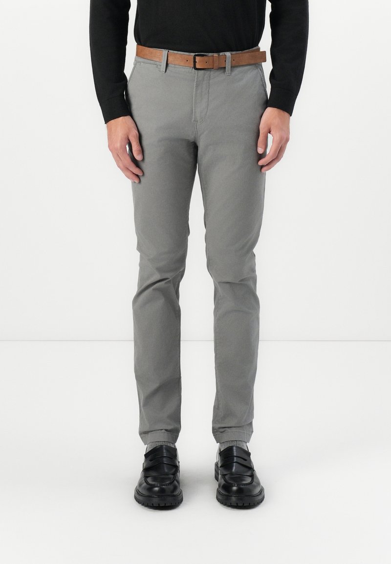 Grijze katoenen broek met een slim fit, met een gladde textuur, voorzakken en een bruine riem. Gecombineerd met zwarte schoenen.