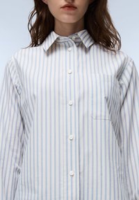 Striped shirt in light blue and white, featuring a button-down collar, front placket with buttons, and a single chest pocket. Cotton blend material.