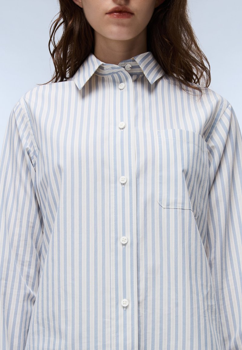 Striped shirt in light blue and white, featuring a button-down collar, front placket with buttons, and a single chest pocket. Cotton blend material.