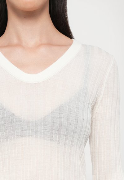 Haut en maille légère, transparente et côtelée en blanc cassé avec un décolleté en V. Présente un motif ton sur ton subtil ressemblant à un soutien-gorge en dessous.