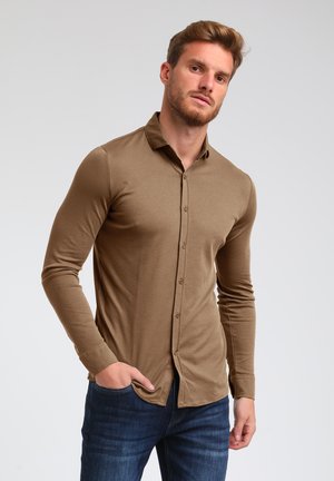 Camisa de manga larga marrón claro con frente abotonado y cuello, confeccionada en una tela suave, combinada con jeans azules.