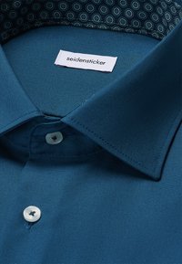 Blaues Hemd mit weißen Knöpfen und gemustertem Innenkragen, mit einem "seidensticker"-Label im Innenkragen.