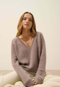 Sweter z dekoltem w kształcie V, z długim rękawem, wykonany z miękkiego, teksturowanego materiału w przytłumionym odcieniu mauve. Manżety i dolna krawędź są ściągaczowe dla dodatkowego detalu.