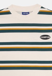 Striped t-shirt in cream, featuring horizontal stripes in dark green and mustard yellow. Includes a black oval "CHAMPION" logo patch.