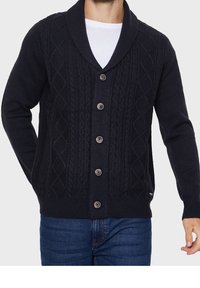 Dark navy cardigan with a shawl collar, textured cable knit patterns, and five buttons down the front. Worn over a white shirt.