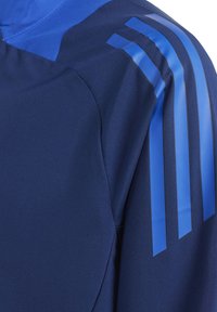 Blaues Sportjackett aus einem glatten, eleganten Stoff mit hohem Kragen und drei auffälligen blauen Streifen, die über die Schulter verlaufen.