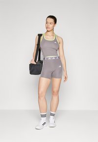 Outfit sportiv gri, compus dintr-un top fără mâneci cu accente verde neon și pantaloni scurți asortati, completat cu o geantă neagră și teniși albi.