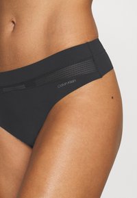 Crne bikini gaćice s glatkom tkaninom i mrežastim panelom na struku, s suptilnim Calvin Klein logotipom.