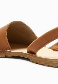 Sandalo in pelle marrone con suola piatta. Presenta fasce larghe e un design semplice. Fodera interna testurizzata e dettagli di cucitura visibili.