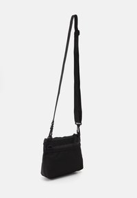 Black crossbody bag made of textured fabric. It features a zippered pocket with a smooth finish and an adjustable strap for customization.