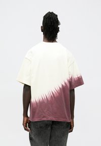 Bawełniany t-shirt z kremową górą i bordowym wzorem tie-dye na dole. Luźny krój, krótkie rękawy i okrągły dekolt.