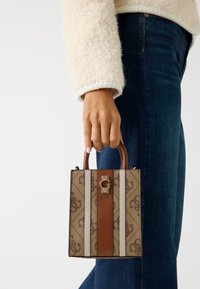 Pequeño bolso rectangular en lona marrón con un patrón y rayas marrones y beige. Presenta un logo dorado, rematado con un asa marrón.