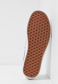 Gummisohle mit strukturiertem, diamantartigem Grip. Weißer Rand entlang des Randes, mit einem schwarzen Oberteil sichtbar. Minimalistisches Design.