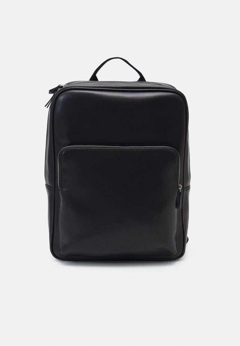 Sac à dos noir avec une texture lisse et mate, doté d'une poche zippée à l'avant, d'une poignée supérieure et d'une forme rectangulaire. Design minimaliste.