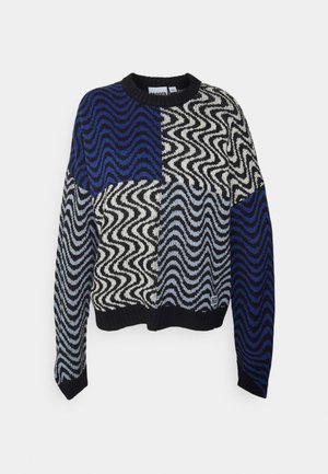 Pull à col rond avec un design patchwork de motifs ondulés en zigzag bleu, noir, blanc et gris, avec poignets et ourlet côtelés.
