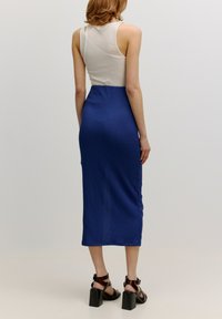 Blaues strukturiertes Midikleid mit taillierter Form, kombiniert mit schwarzen Sandalen mit Blockabsatz. Oben hat es einen cremefarbenen Tank-Style.
