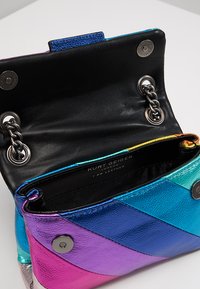 Bolso de cuero multicolor con un patrón de Chevron en púrpura, azul y plata. Presenta un interior negro, cierre a presión y herrajes metálicos.