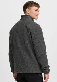Grå fleece genser med høy krage, strukturert overflate og elastiske mansjetter. Har rett avslutning og minimale detaljert i maskinvare.