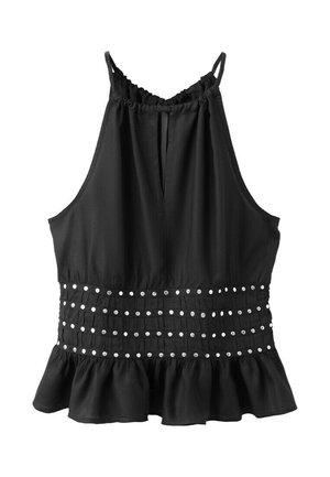 Femme aux longs cheveux portant un haut noir sans manches avec des clous, un short en jean gris clair et des sandales noires à lanières, debout sur fond blanc.