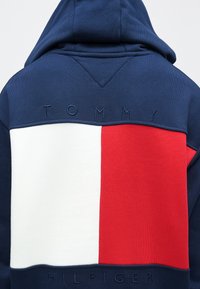 Μπλε σκούρο φούτερ με κόκκινα και λευκά μπλοκ σχέδια. Το «TOMMY» είναι κεντημένο στο πάνω μέρος και το «HILFIGER» στο κάτω μέρος. Μαλακό βαμβακερό ύφασμα, άνετη εφαρμογή.