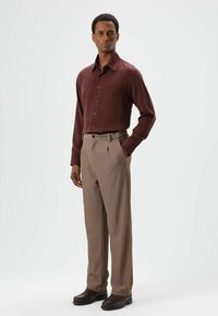 Chemise bordeaux à manches longues avec boutons, associée à un pantalon plissé marron clair ; les deux ont une texture lisse. Chaussures marron complètent la tenue.