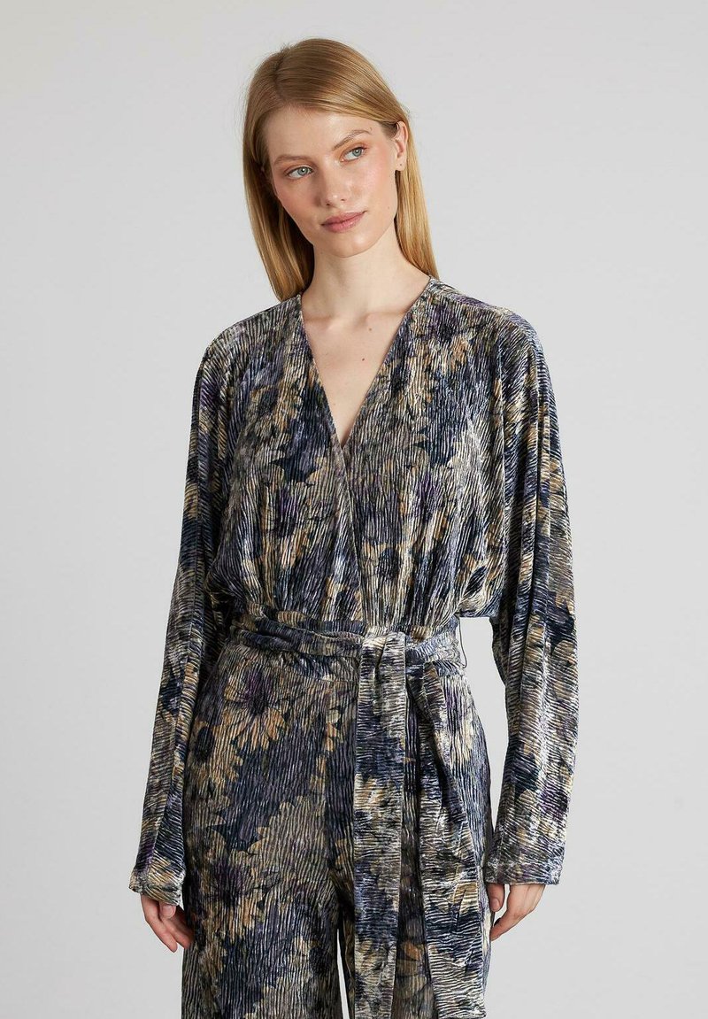 Vestido envolvente de manga larga en tejido estampado con un acabado brillante. La paleta de colores incluye marino, crema y dorado, con una superficie texturizada y un cinturón atado en la cintura.