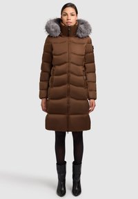 Rjava vatirana bunda z ovratnikom s krznom, ki ima prešito zasnovo in zadrgo, kombinirana s črnimi gležnjarji in nogavicami.