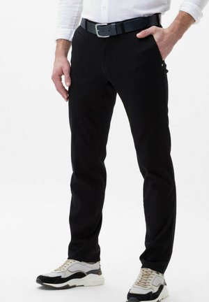 Schwarze Hosen aus einem glatten Material, im Slim-Fit-Schnitt, mit Taschen und einem schwarzen Gürtel. Dazu werden hellfarbene Sneakers getragen.