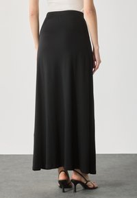 Zwarte, lange maxi-rok van zachte stof, met een elastische tailleband. Gecombineerd met open teen hoge hakken.
