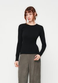 Pull noir à manches longues au design ajusté avec un col rond, associé à un pantalon en velours côtelé gris à jambes larges, présentant une texture côtelée.