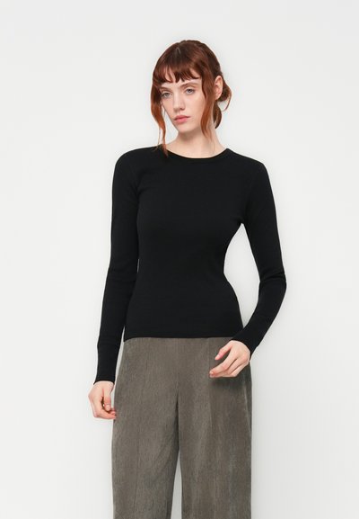 Pull noir à manches longues au design ajusté avec un col rond, associé à un pantalon en velours côtelé gris à jambes larges, présentant une texture côtelée.